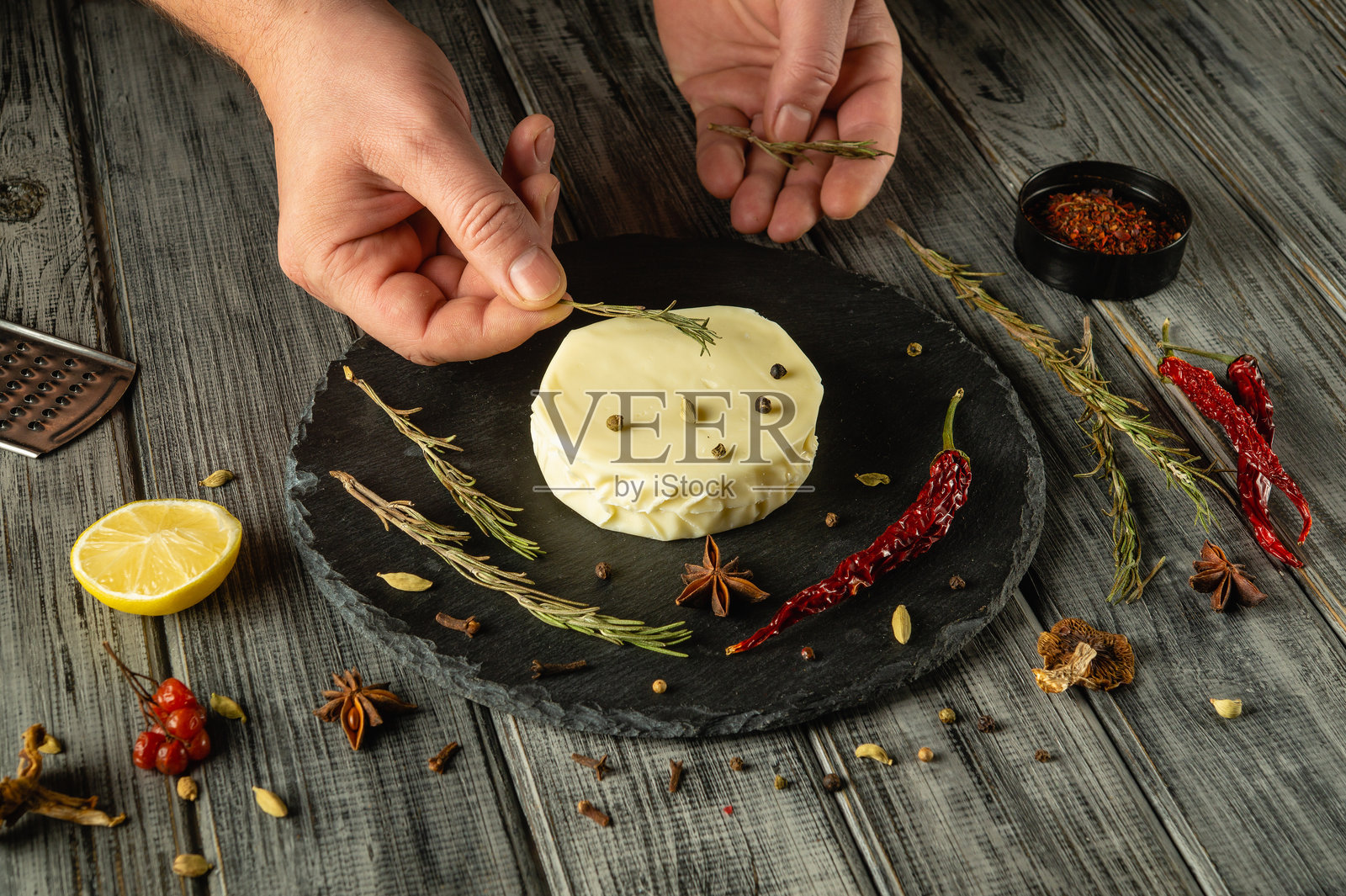 双手精心摆放新鲜的香草和香料,围绕着一块奶油奶酪。质朴的木桌增添了温馨的氛围,非常适合烹饪创作或聚会。照片摄影图片