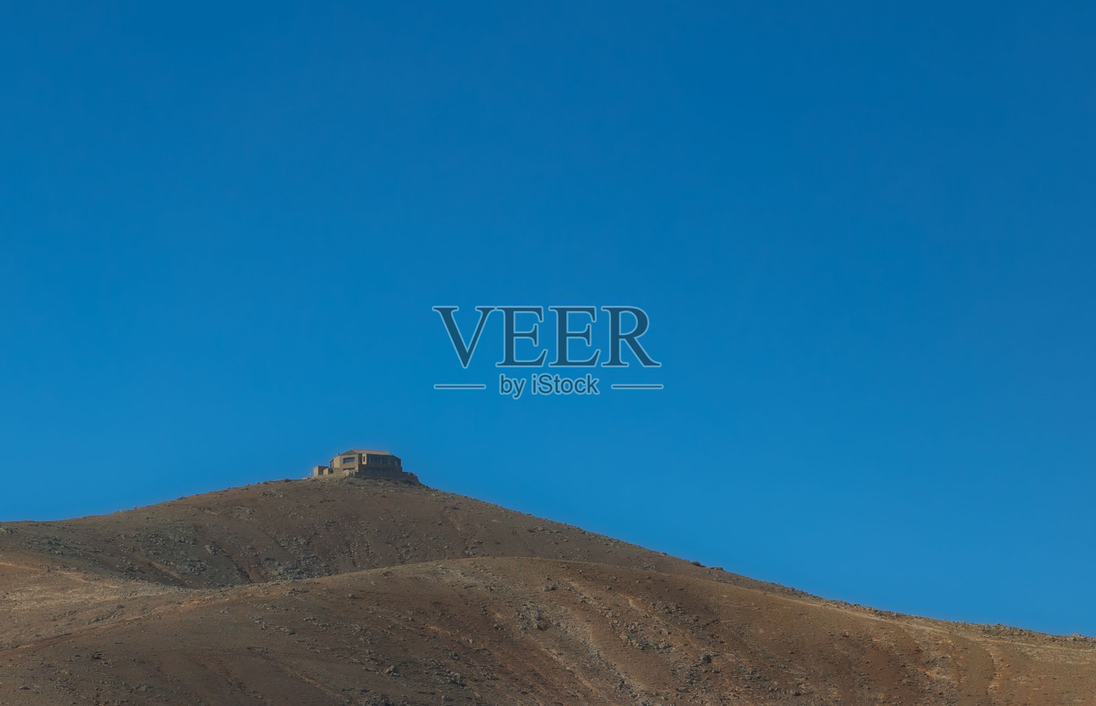 荒凉山丘上的孤独建筑,映衬着晴朗的蓝天。照片摄影图片