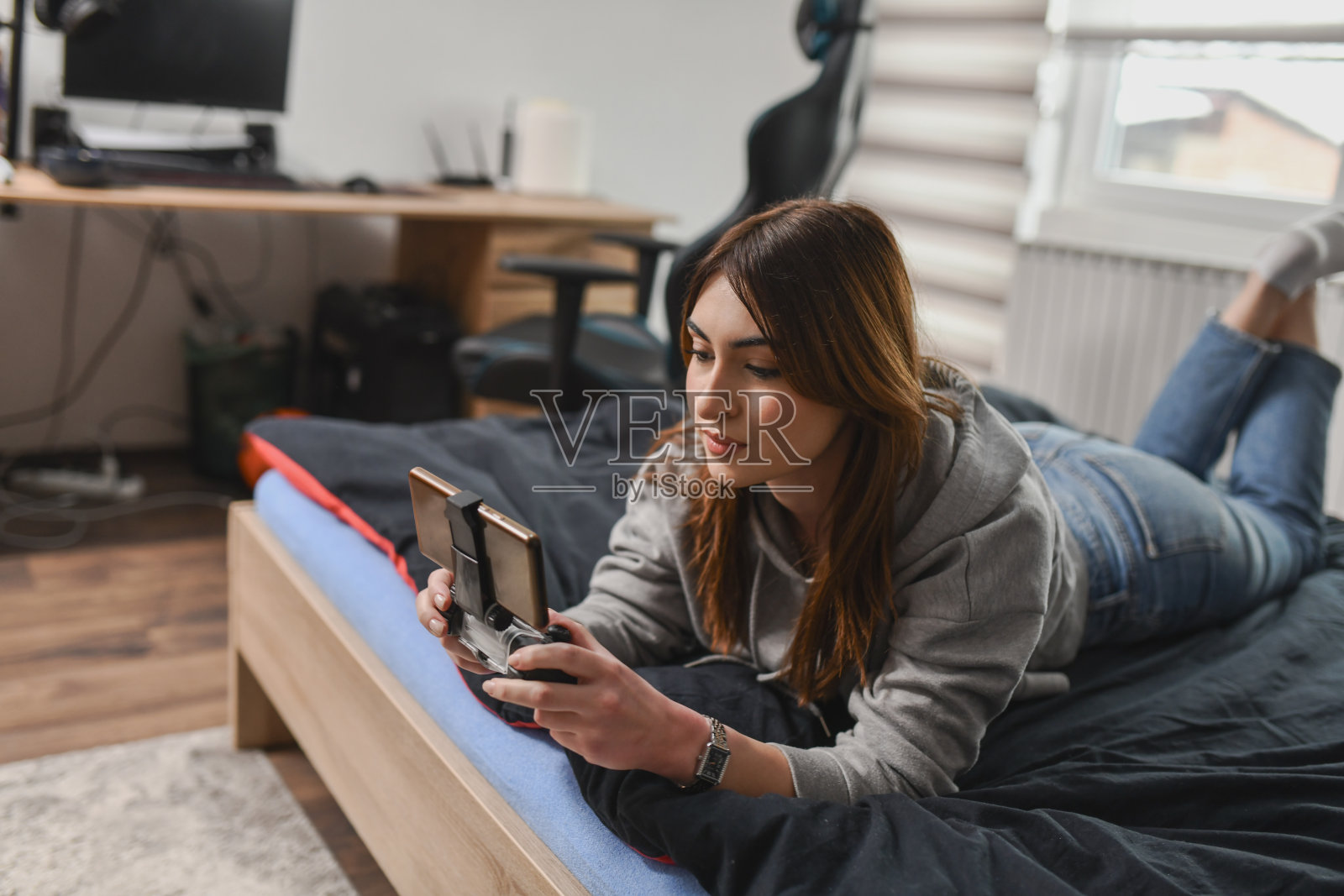 专注的女性躺在床上,眼睛紧盯着手机屏幕和视频游戏。照片摄影图片