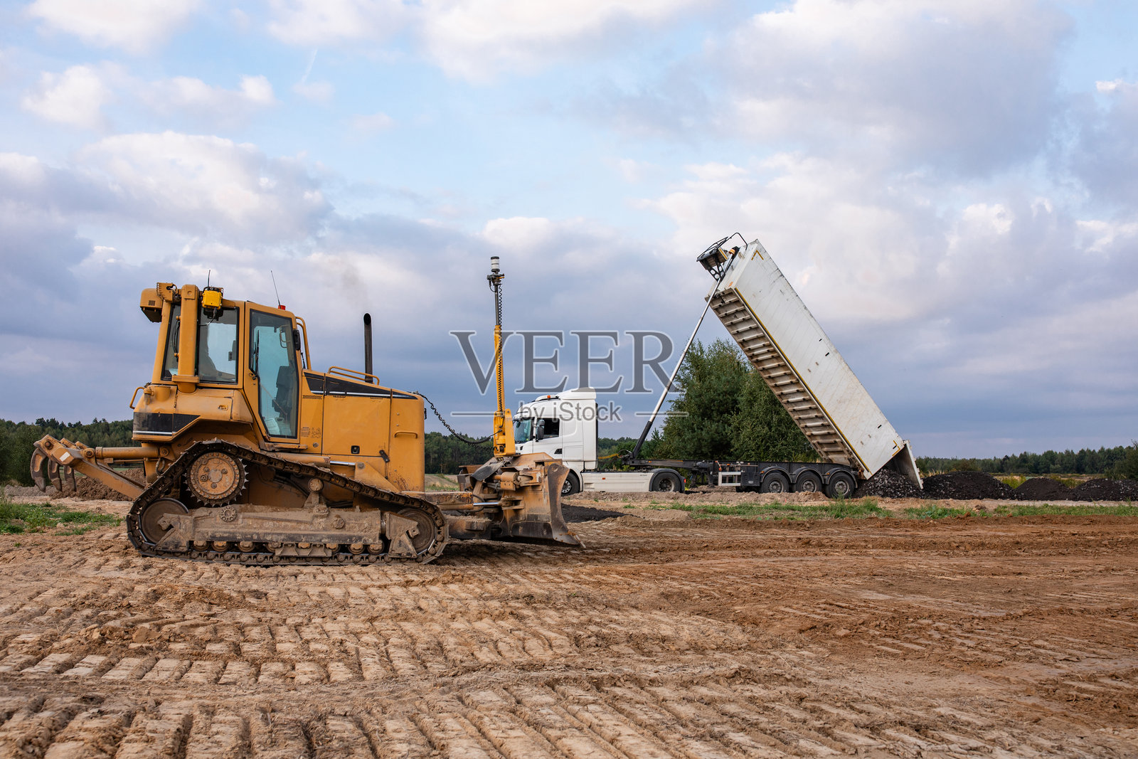 采石场施工现场的履带式推土机和自卸车。现代强大的土方工程设备。施工现场。重型推土机和自卸车正在作业。建筑机械。照片摄影图片