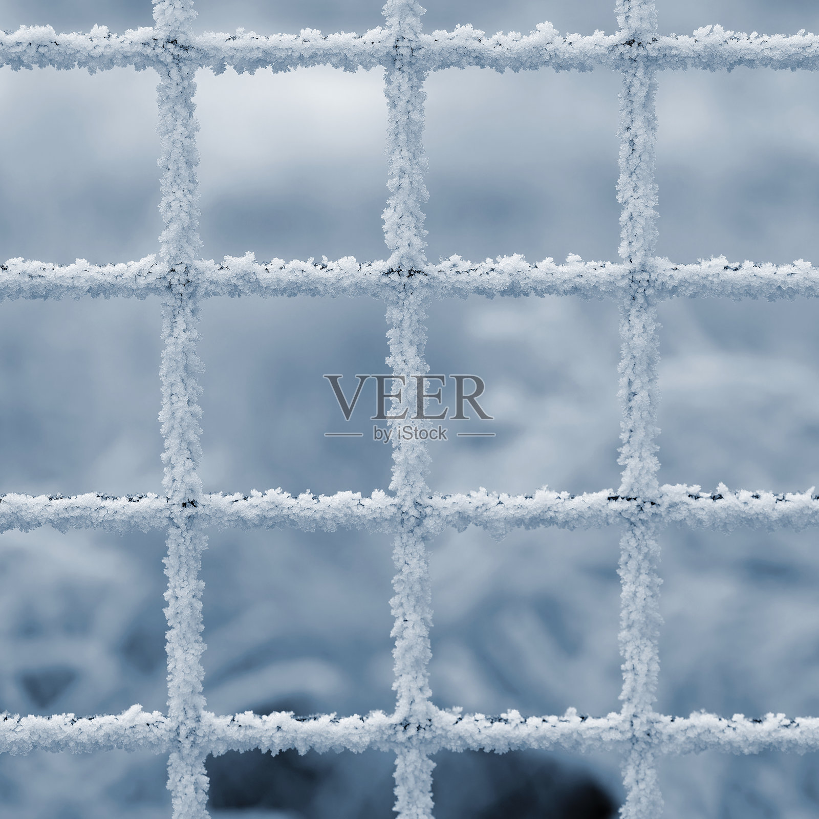 一个极简主义的特写镜头,展示了覆盖着冰晶的金属网格,背景是柔和模糊的冬季景色。霜的复杂图案突显了网格的几何对称性,营造出宁静而抽象的冬季构图。照片摄影图片