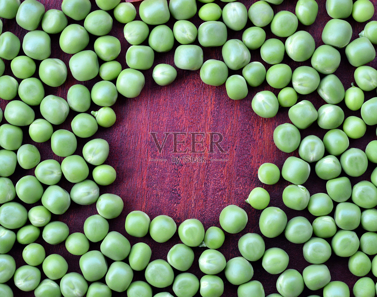 剥皮的绿色豌豆 - 有机新鲜健康的蔬菜沙拉,艺术性地摆放在棕色木质表面上,如切菜板,水平背景中间有圆形留白空间。照片摄影图片