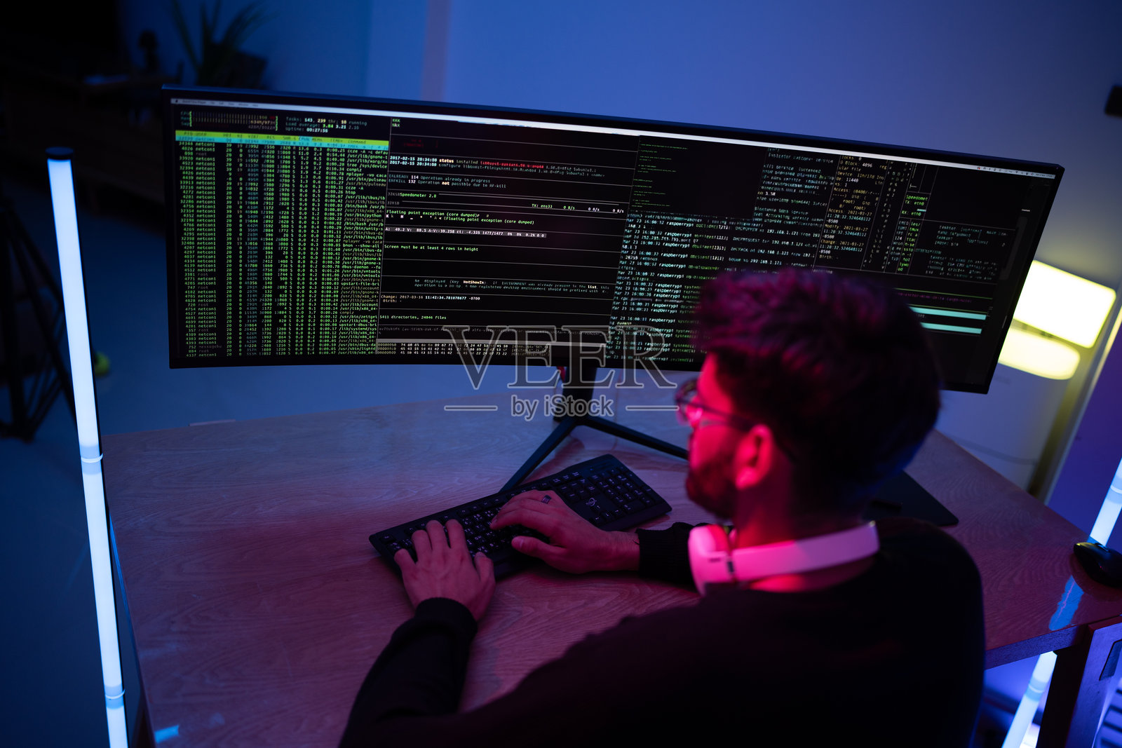 专注的程序员在现代工作空间中熬夜工作,双屏显示代码和数据分析。照片摄影图片