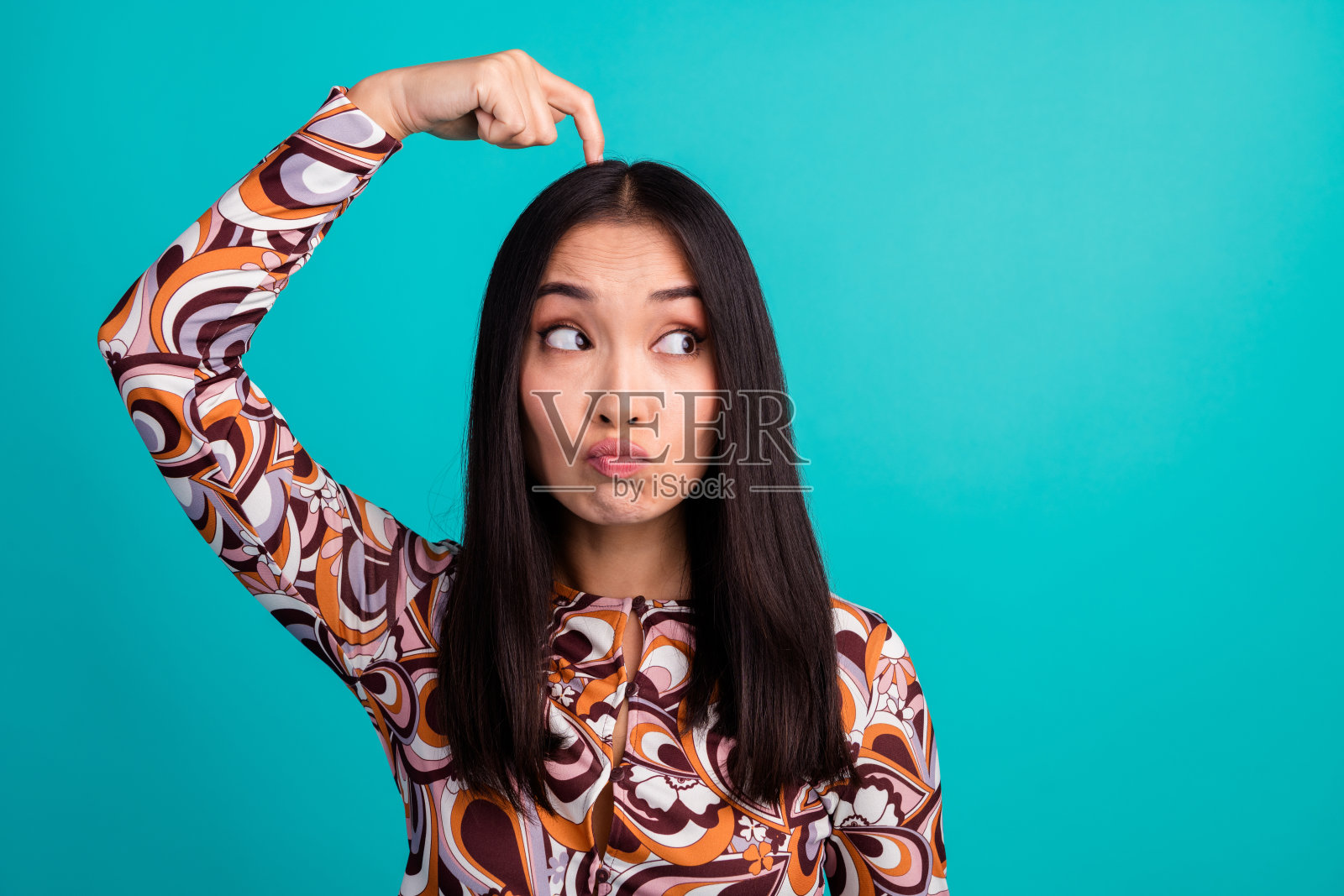 年轻女孩的肖像,抓着头,目光空洞,穿着上衣,背景为青绿色。照片摄影图片