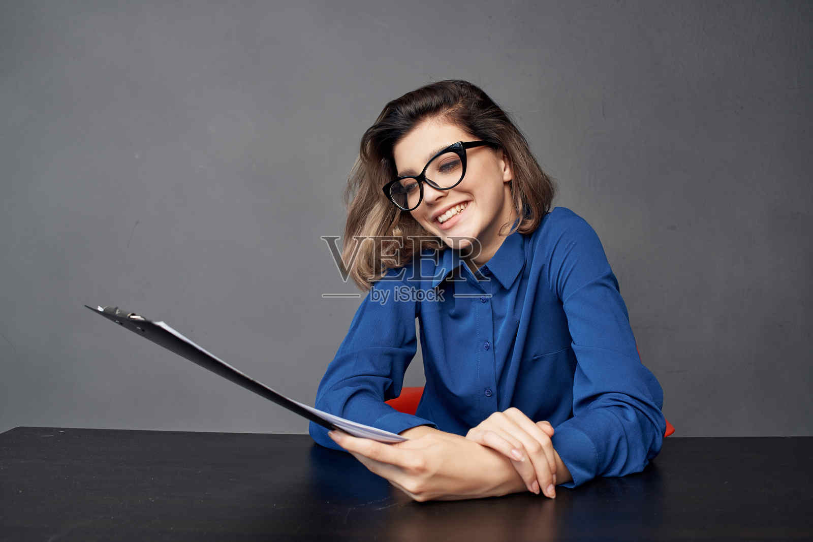 穿蓝色衬衫的女人坐在桌子旁,手中拿着文件,留白空间。照片摄影图片