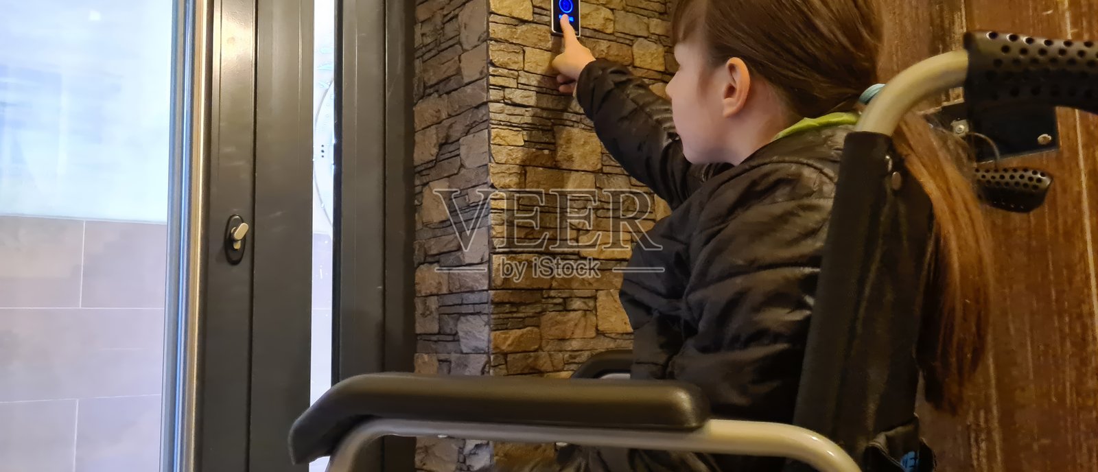 坐在轮椅上的残疾女孩按下无障碍入口按钮照片摄影图片