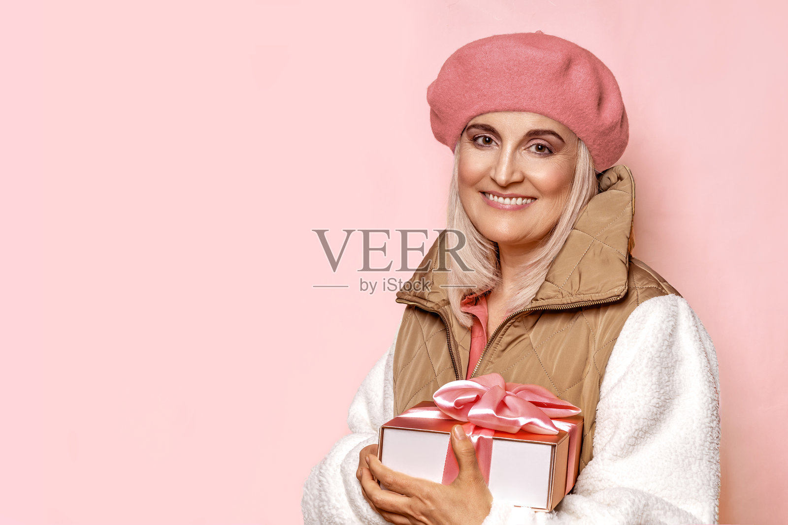 一位五十多岁美丽女性的肖像,穿着米色和粉色的衣服,背景为粉色。特写肖像,留有文字和空白空间。照片摄影图片