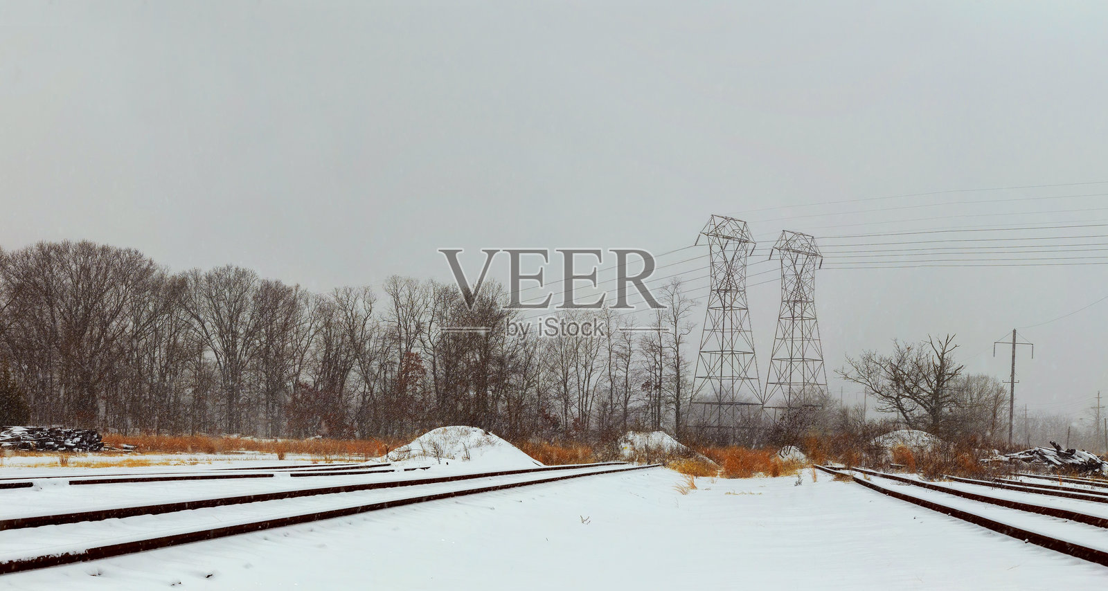 被雪覆盖的铁路轨道延伸穿过宁静的冬季风景,背景中有电线。照片摄影图片