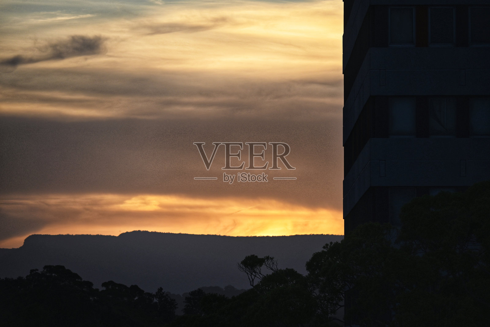 傍晚天空中的色彩。澳大利亚新南威尔士州的伍伦贡。城市天际线,单元楼和商业建筑的尖锐边缘与背景和前景中的城市粗糙感形成鲜明对比。照片摄影图片