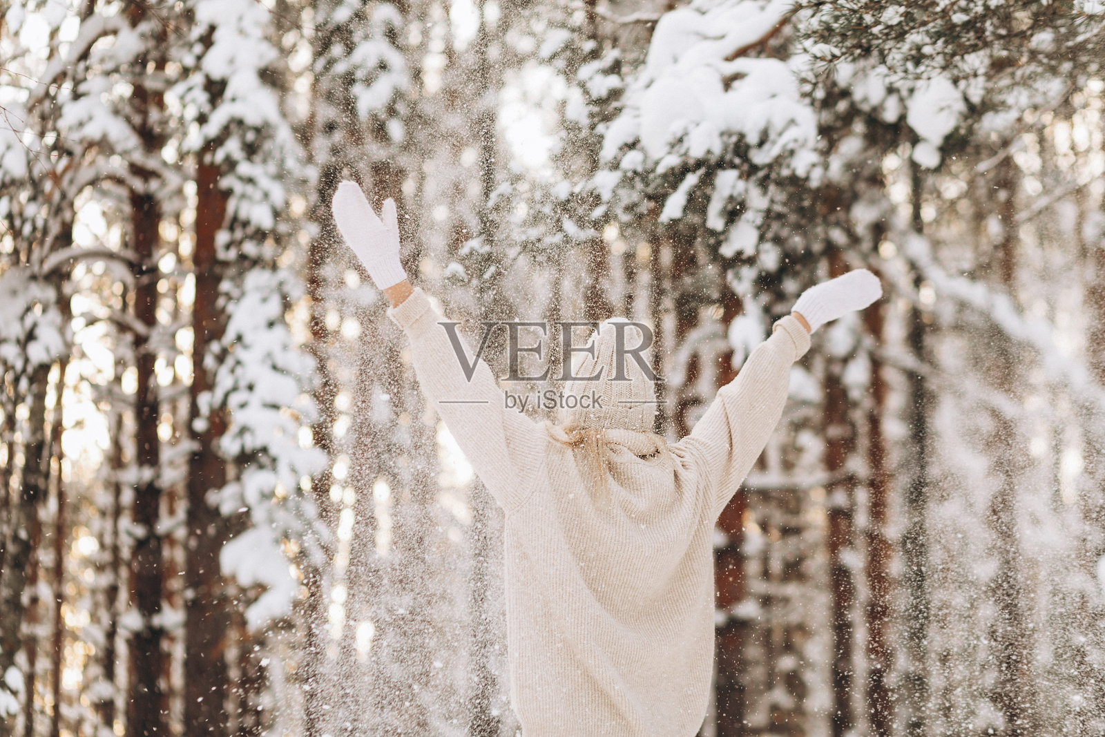 年轻女性背影在冬季森林中愉快地抛起雪花,背景中飘落着雪花。照片摄影图片