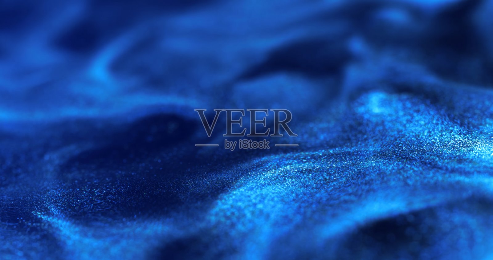 丰富而深邃的蓝色表面,带有旋涡状的波浪图案和闪烁的细颗粒质感。照片摄影图片