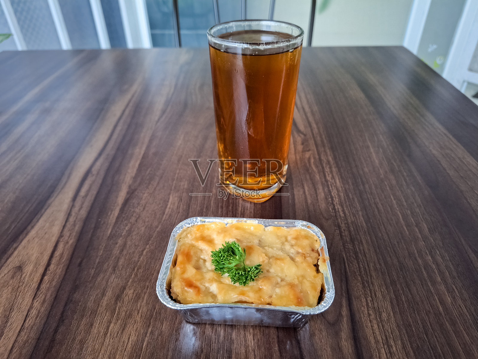 通心粉烤菜是一道由意大利面、通心粉、肉类、香肠、鸡蛋、洋葱、土豆、黄油、牛奶和奶酪制成的烤菜。玻璃杯中的新鲜茶。食品和饮料菜单。照片摄影图片