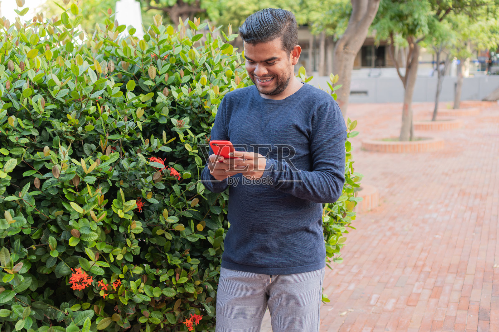 年轻的拉丁裔男子在公园里使用手机并微笑照片摄影图片