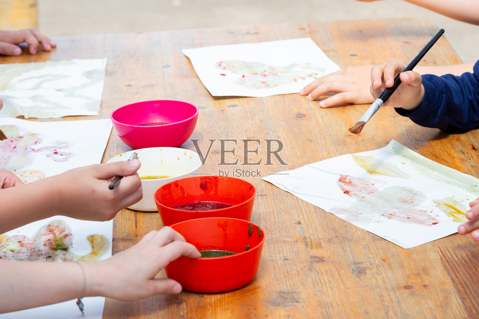 孩子们坐在桌子旁,用红色颜料的碗进行绘画照片摄影图片