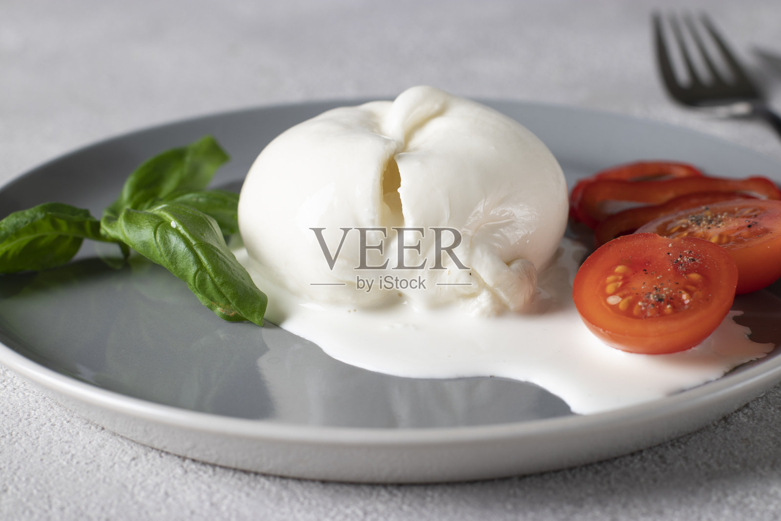 意大利布拉塔奶酪放在灰色盘子上,配有罗勒和樱桃番茄照片摄影图片