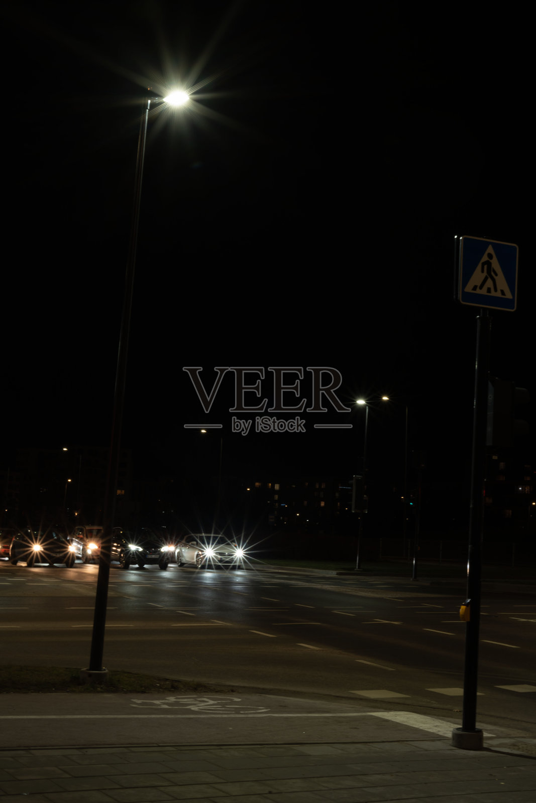 城市夜景,灯光照亮的街道上,车头灯的光辉在沥青上投射出倒影,行人过街道的标志在明亮的路灯下清晰可见。照片摄影图片