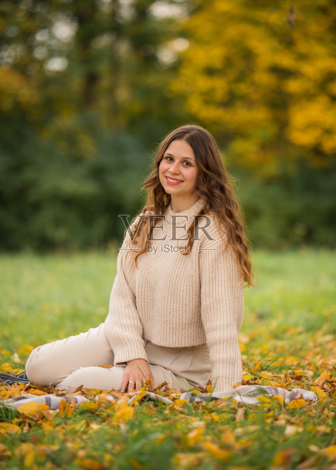 一个可爱的女孩长发披肩,坐在秋天的公园里。周围落满了明亮的黄色树叶。照片摄影图片