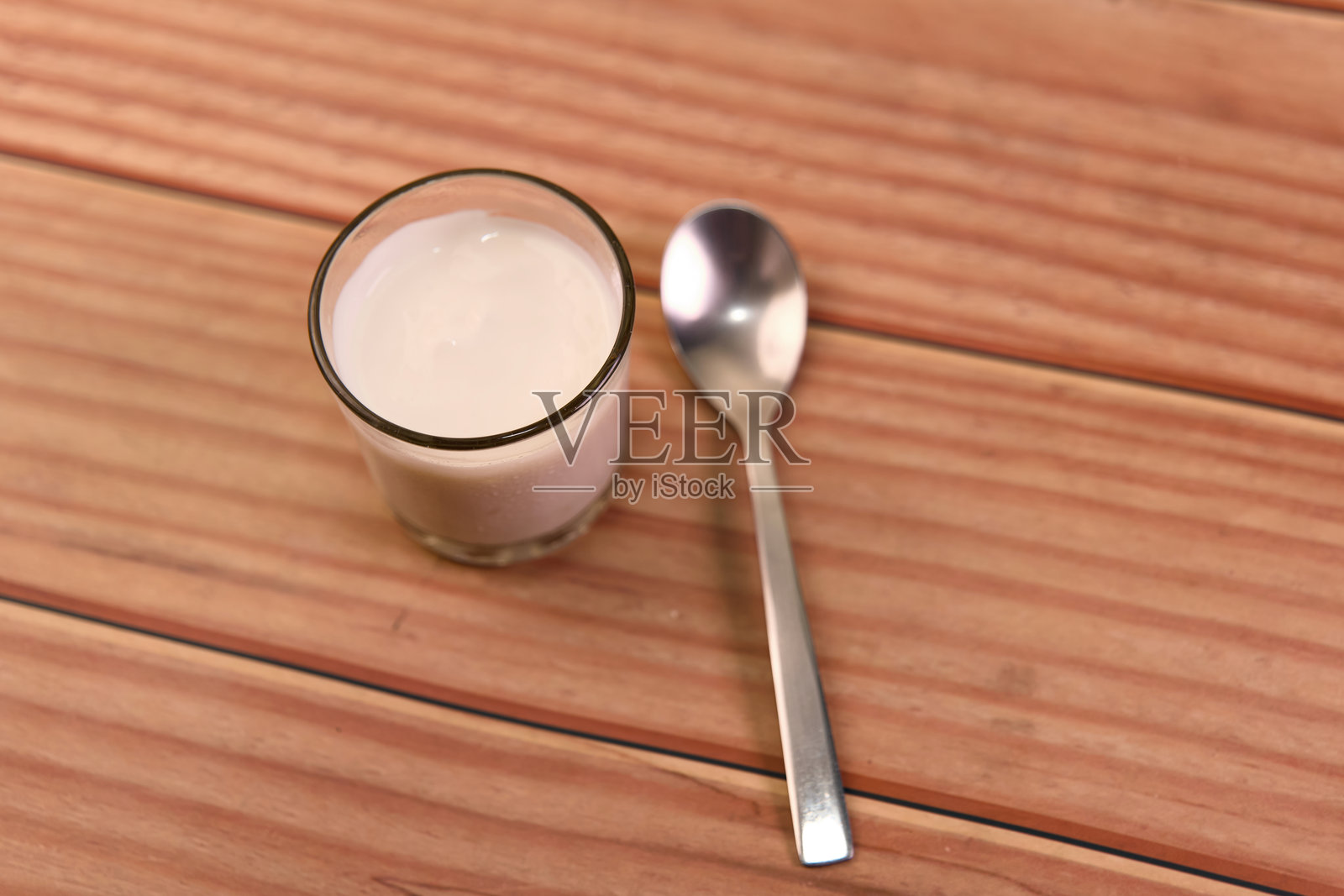 一杯牛奶放在木桌上,旁边有一把勺子。照片摄影图片