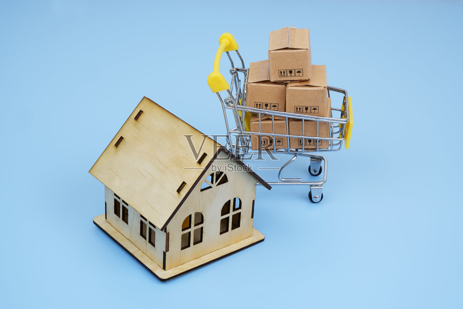 购物车里装满了纸箱和一个房屋模型,背景为蓝色。照片摄影图片