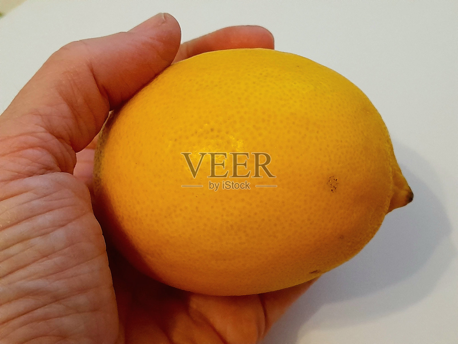 手握一个完整的柠檬,背景为白色。照片摄影图片