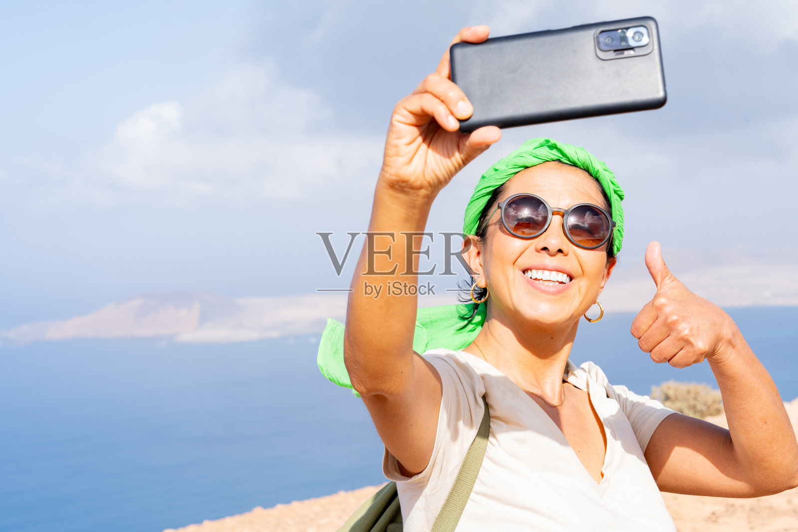 快乐的游客在阳光明媚的兰萨罗特岛拍自拍,竖起大拇指,记录假期回忆。照片摄影图片