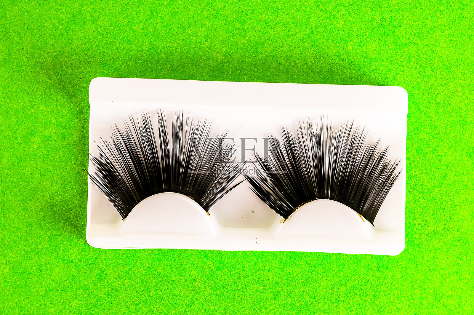 两只假睫毛展示在绿色表面上照片摄影图片