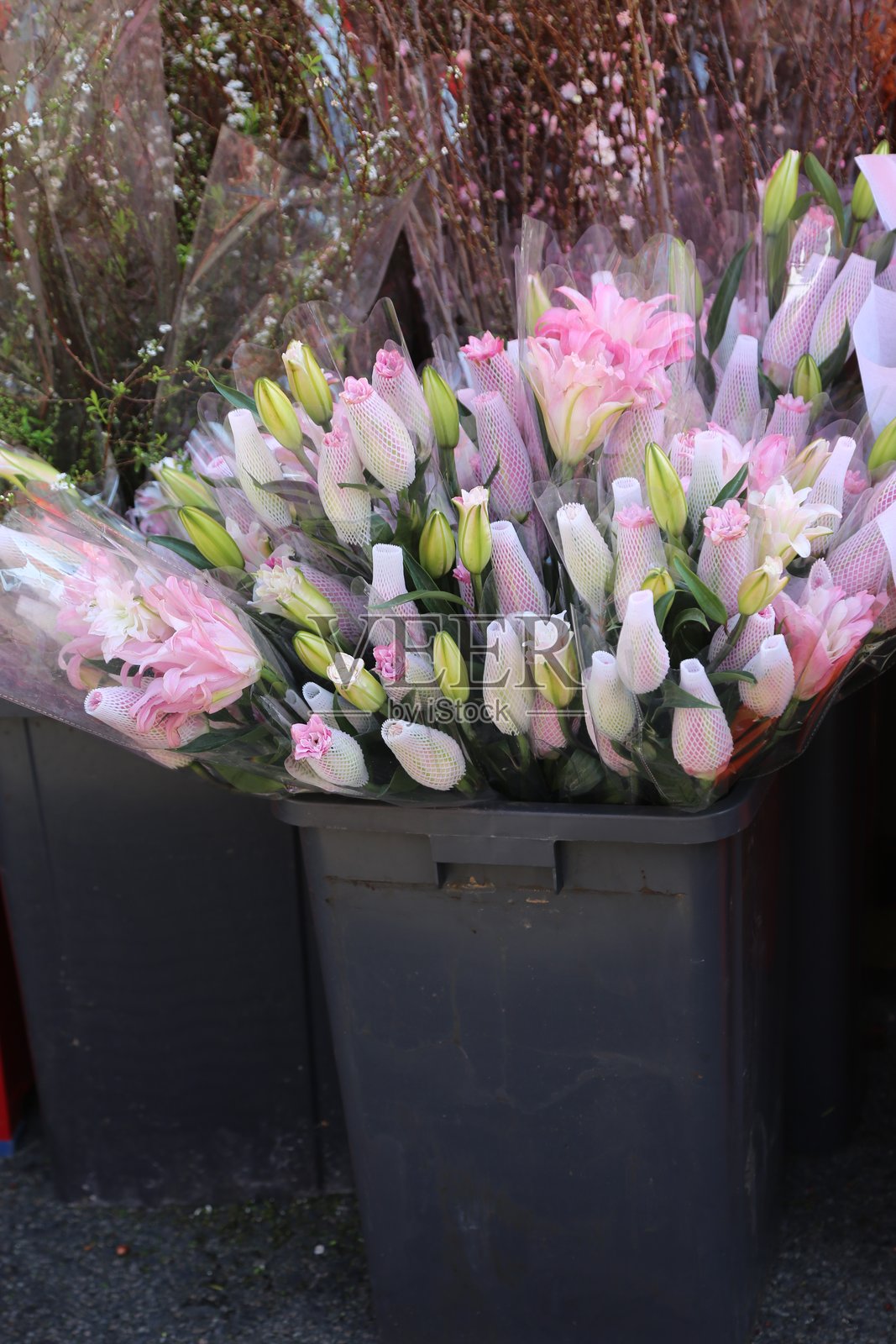 一大束粉色和白色的郁金香、玫瑰和百合用塑料包装放在户外市场的灰色花卉箱上。照片摄影图片