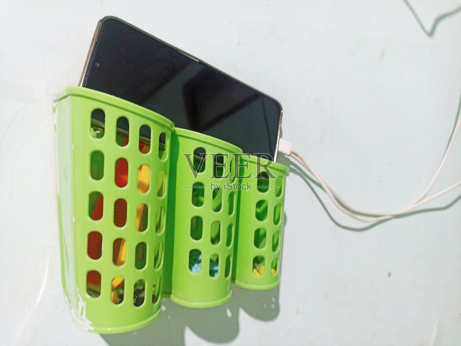 正在充电的手机存放在墙上安装的塑料支架中。照片摄影图片