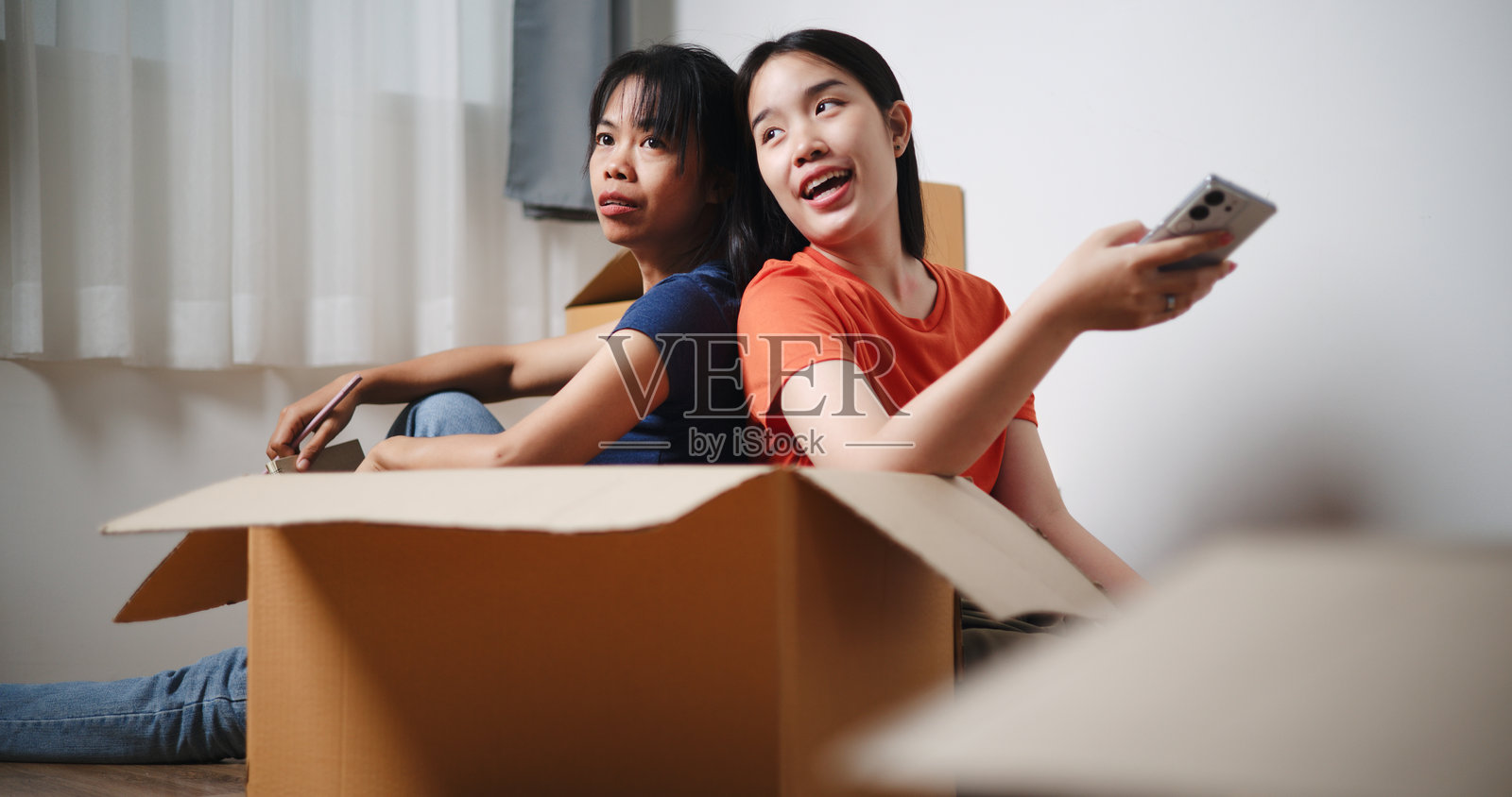 两个快乐的兄妹背靠背坐着,互相帮助设计房间的装饰。照片摄影图片