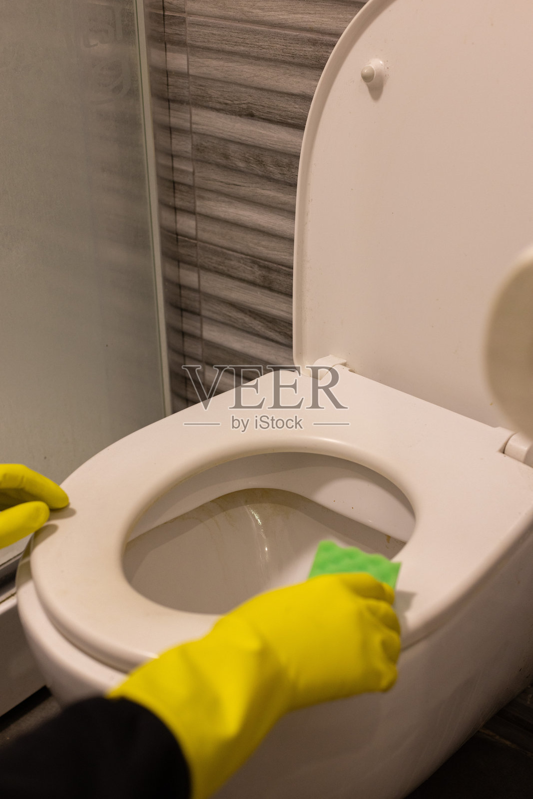 戴着黄色橡胶手套的手用海绵清洁马桶。照片摄影图片