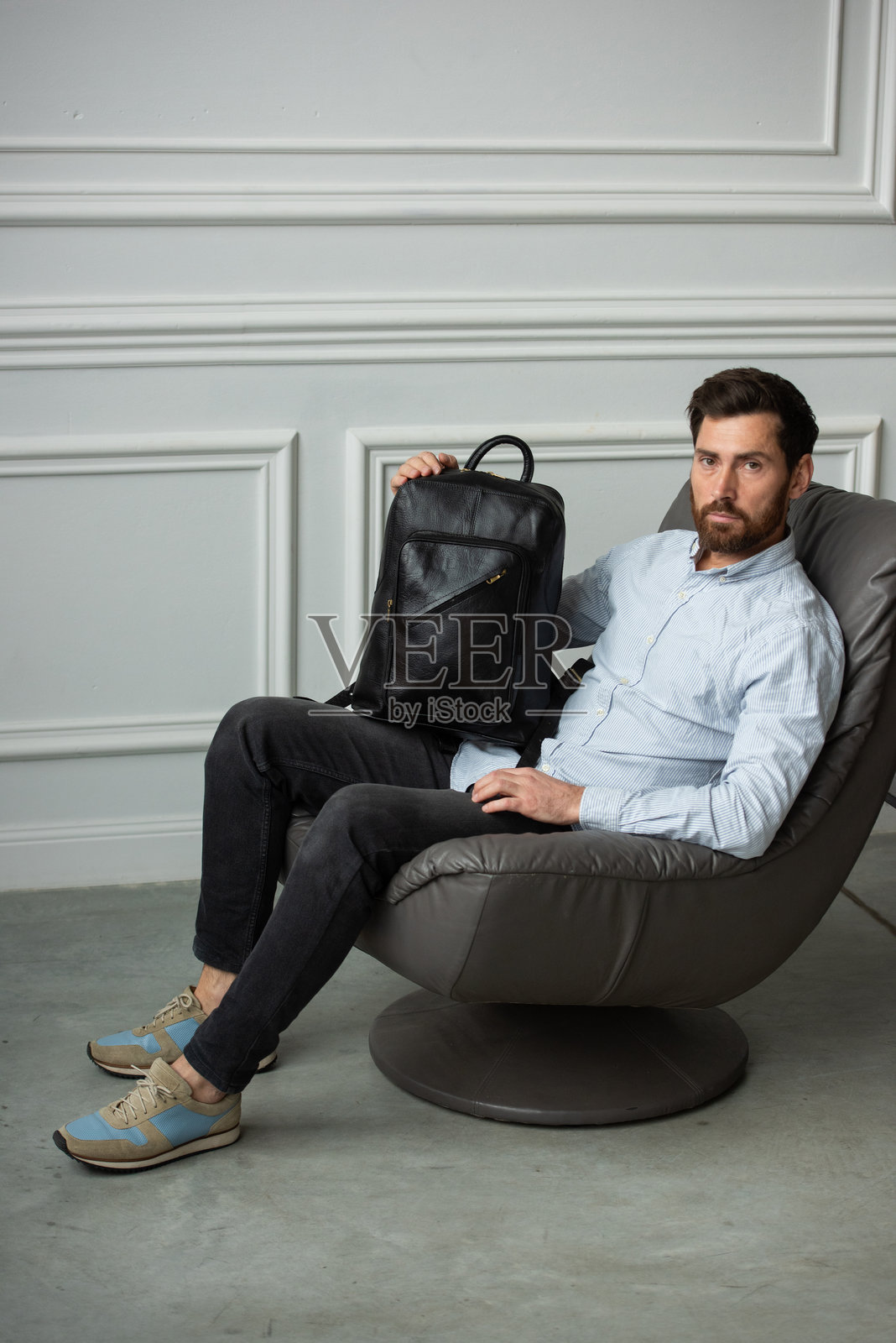 一个男人舒适地坐在椅子上,旁边放着一个皮革背包。照片摄影图片