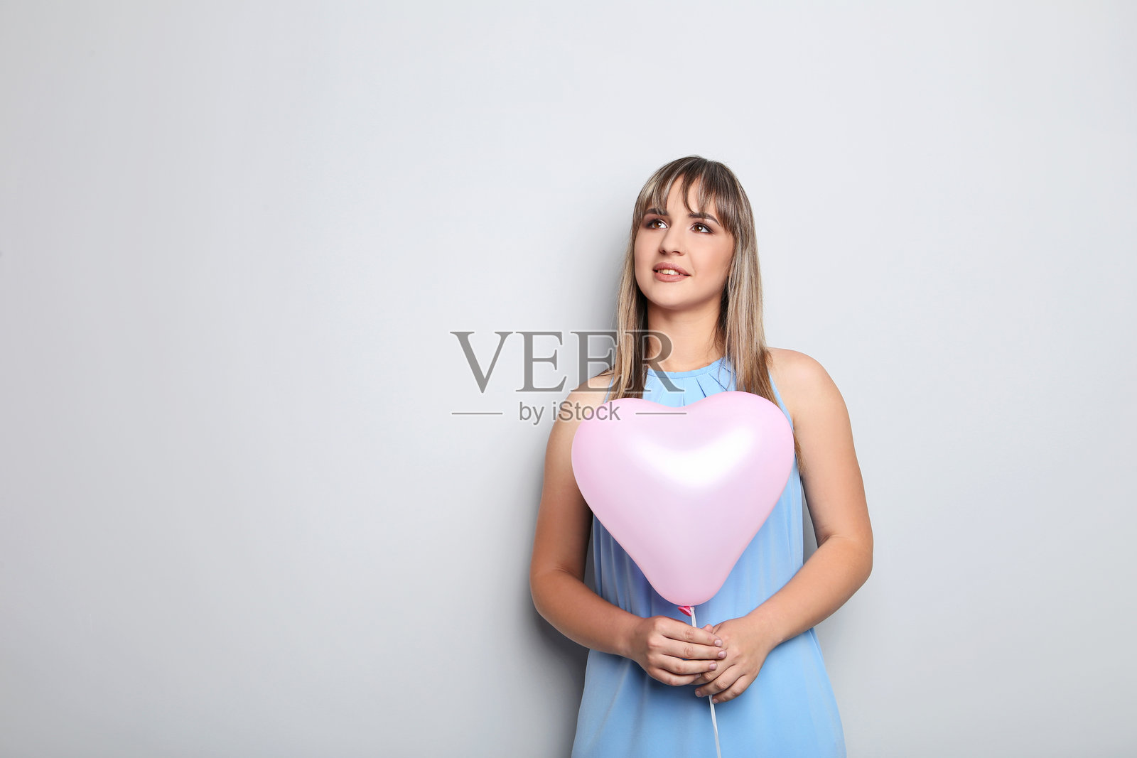 年轻女性手持粉色心形气球,背景为灰色照片摄影图片