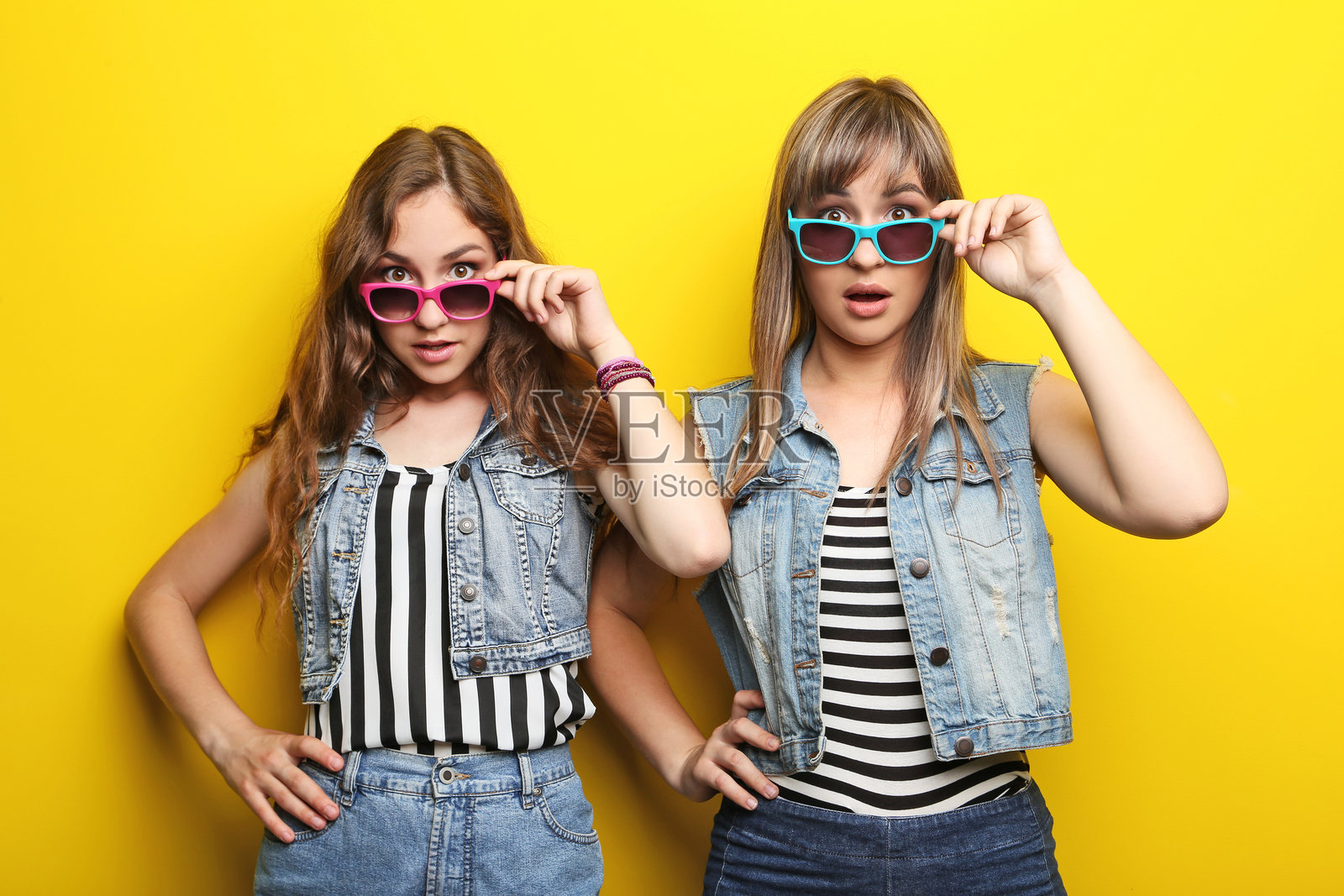 两位年轻女性佩戴太阳镜,背景为黄色照片摄影图片