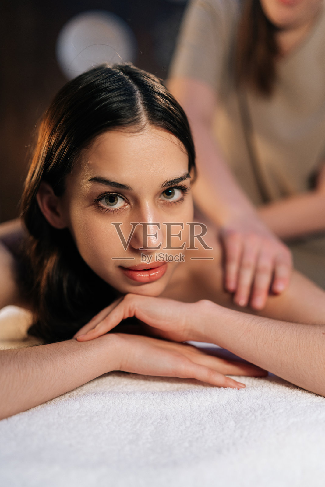 年轻女性在美容水疗中心放松,享受手部按摩,面朝镜头。专业按摩师正在为放松的女性客户进行背部按摩。照片摄影图片