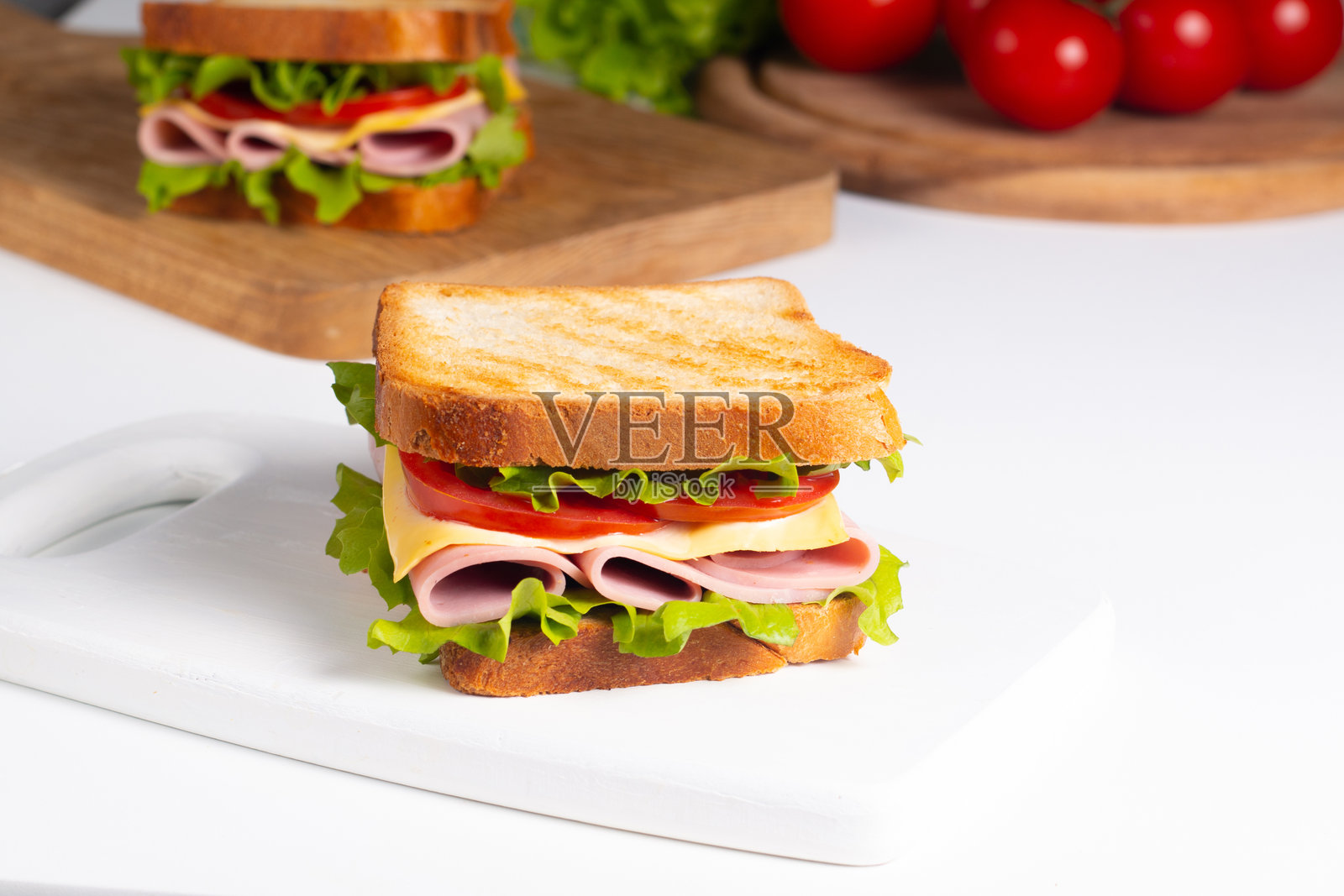 特写两份夹有培根、萨拉米香肠、意大利火腿和新鲜蔬菜的三明治,放在乡村风格的木砧板上。俱乐部三明治概念照片摄影图片