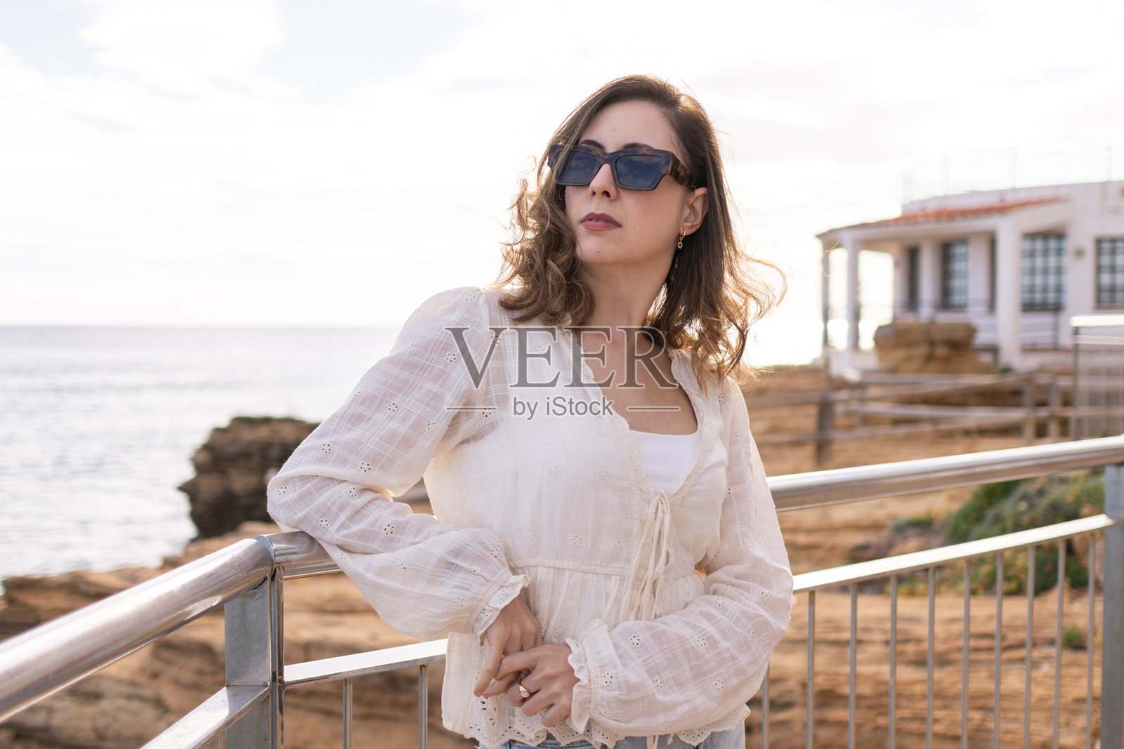 美丽的成年白人女性,长发,戴着太阳镜,神情严肃而沉思,在阳光明媚的日子里凝视着海面上的地平线。照片摄影图片