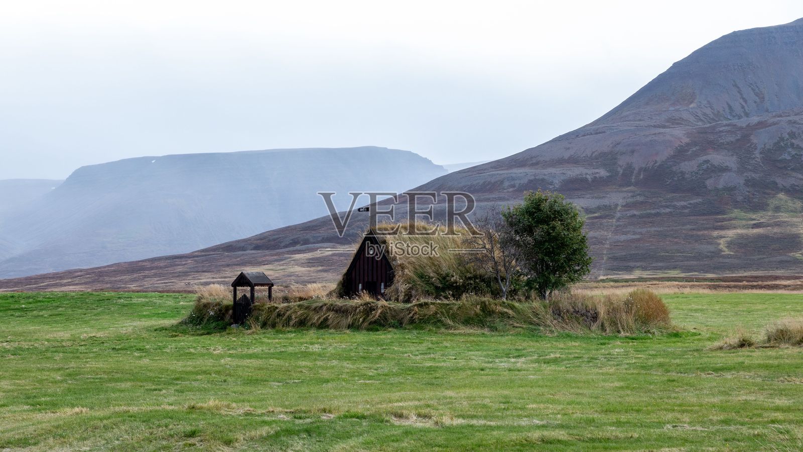 冰岛一座乡村草屋,四周环绕着草地和山脉,天空多云。照片摄影图片