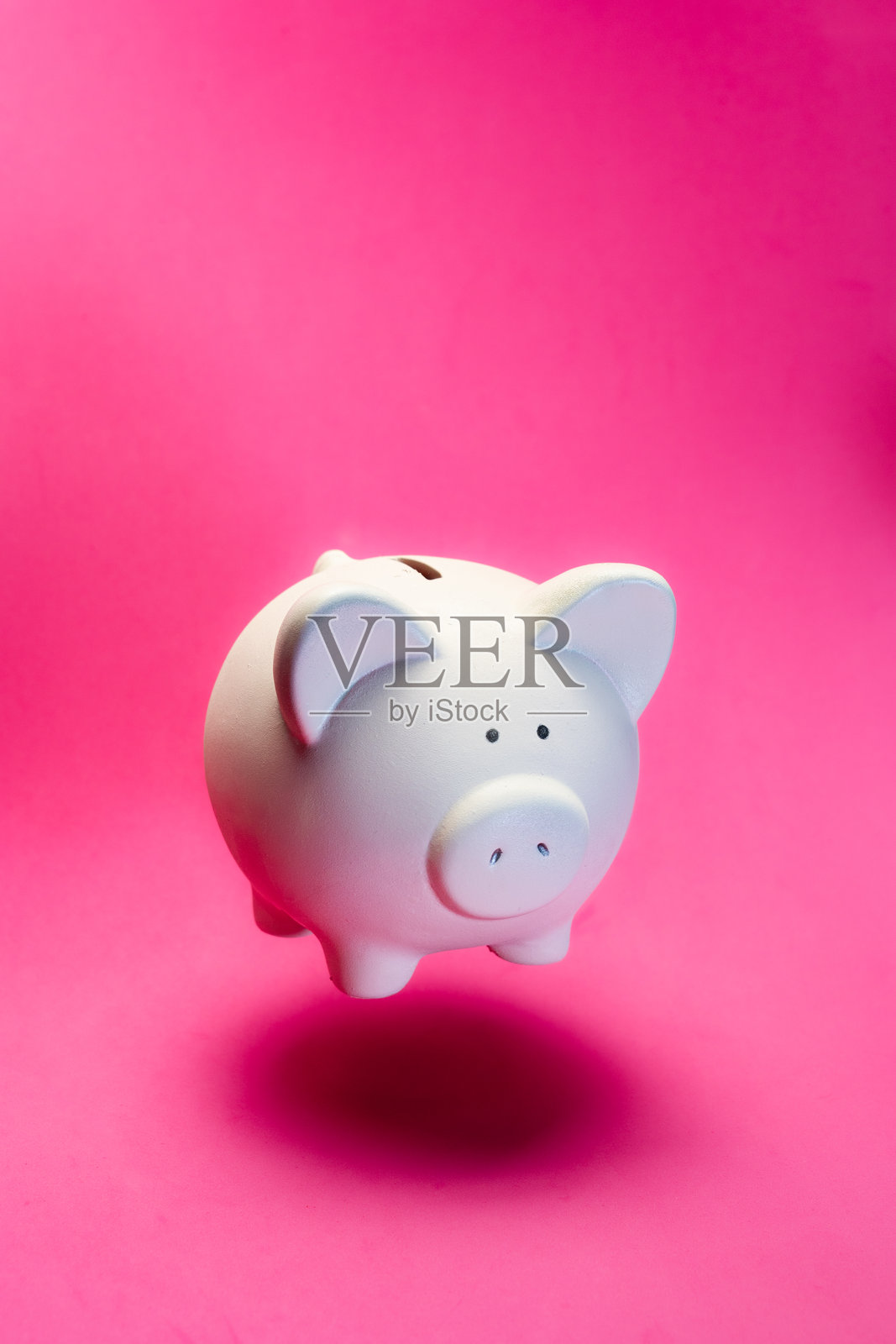 白色陶瓷储蓄罐站在明亮的粉色背景前,象征着财务规划和财富积累照片摄影图片