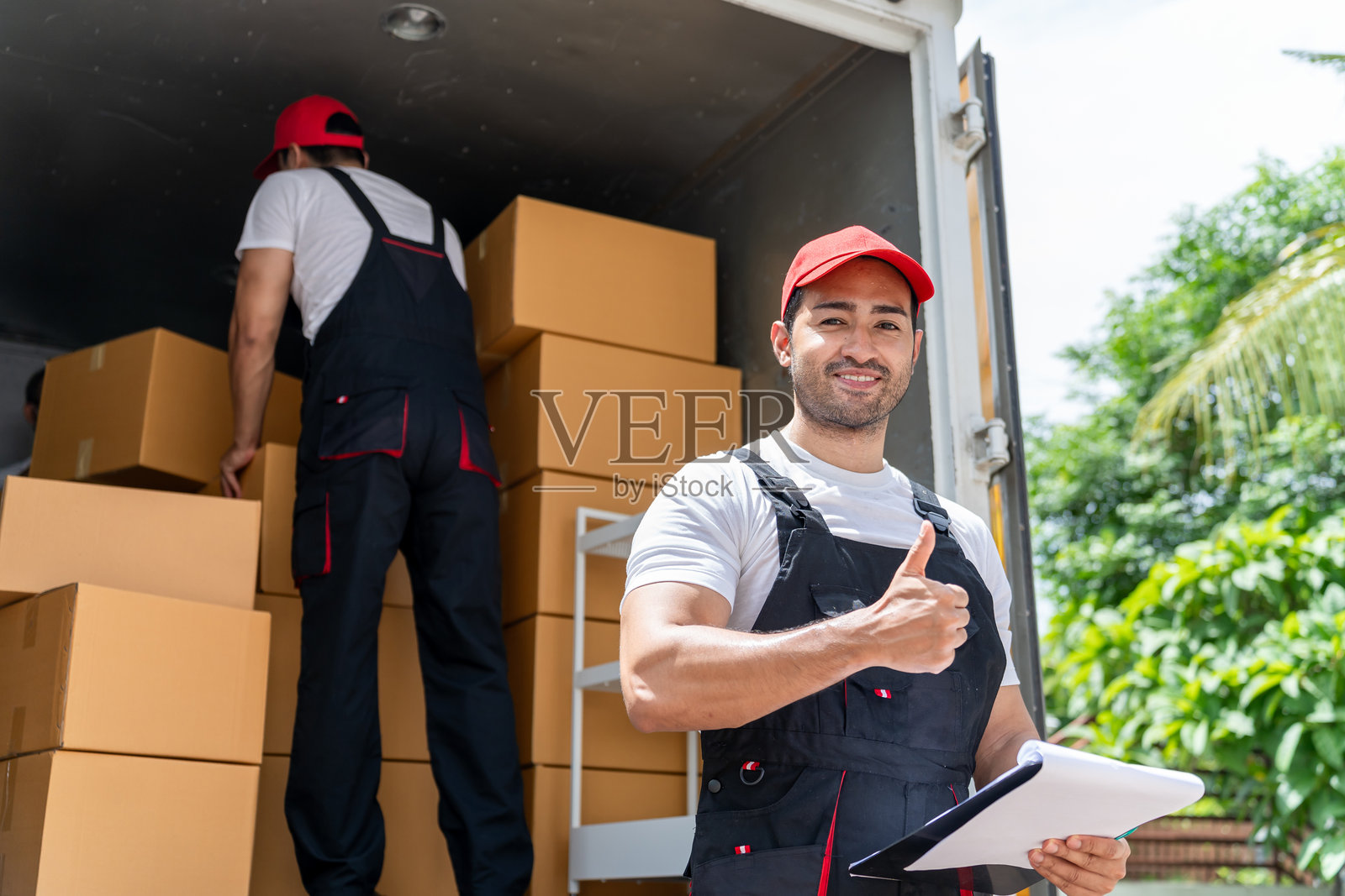 白人快递员将包裹送到家门口的肖像。吸引人的快递员在工作,正在从汽车上装载纸箱并看向镜头。照片摄影图片