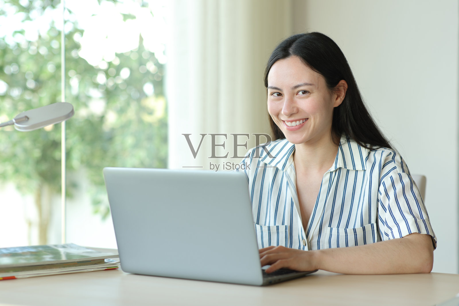 快乐的亚洲女性正在使用笔记本电脑,朝着你微笑。照片摄影图片