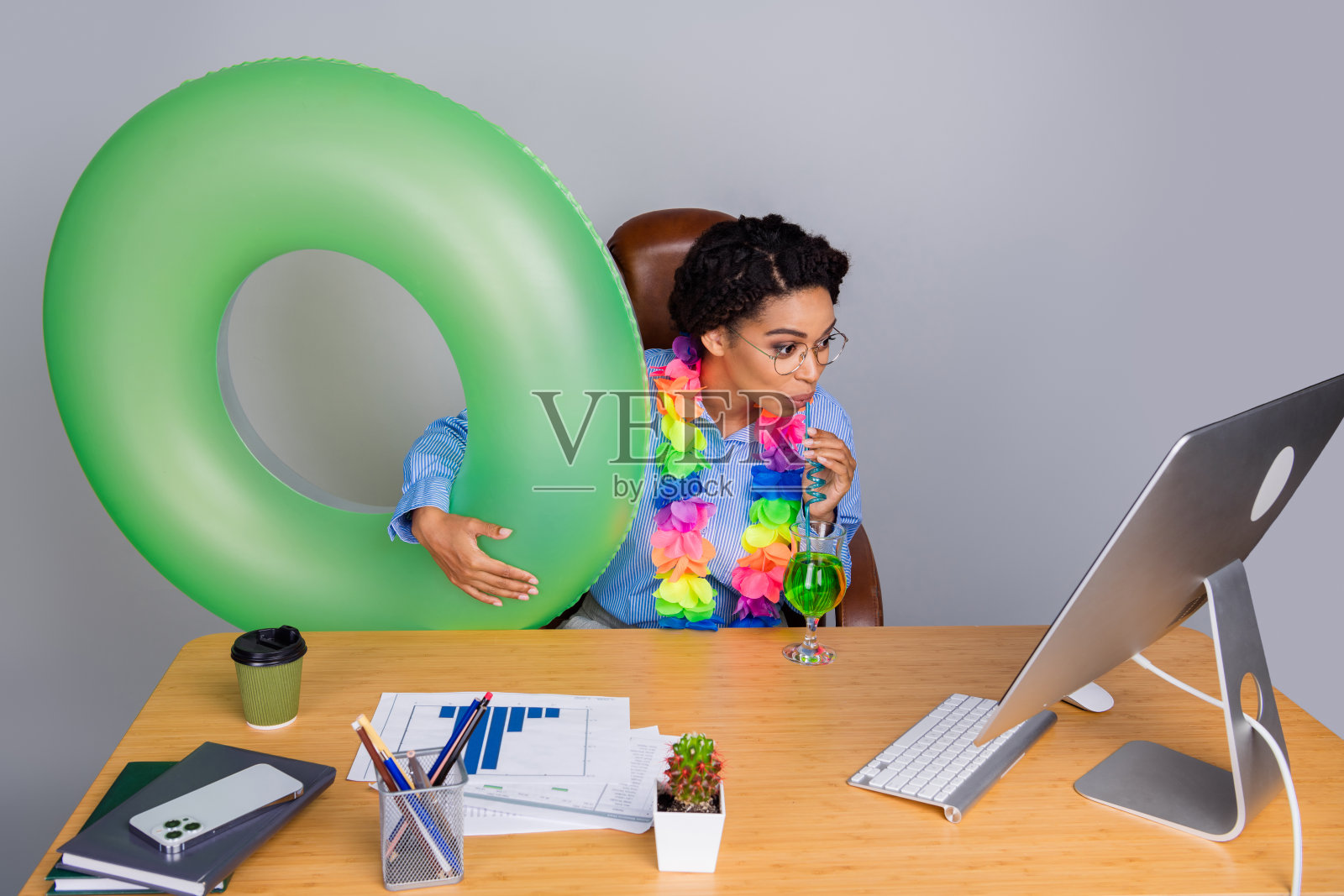 年轻的非裔美国女商人与绿色浮标和五彩花环在办公室桌前享受热带饮品。照片摄影图片