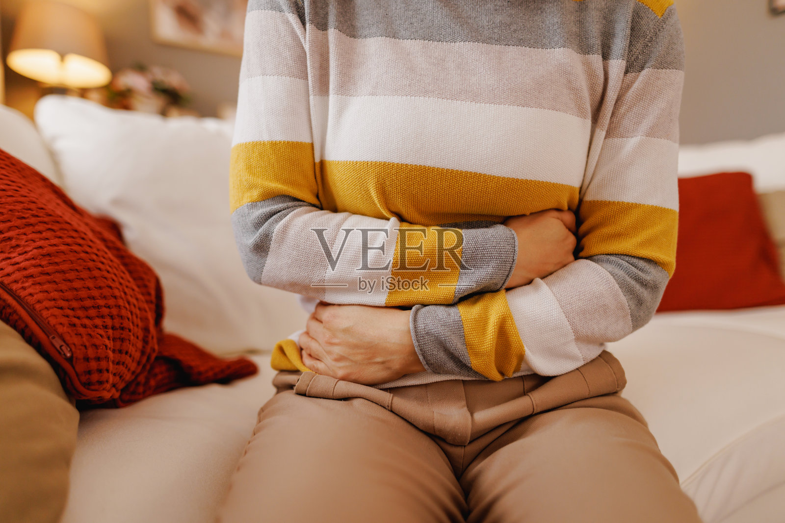 女人坐在家里的沙发上感到腹痛照片摄影图片