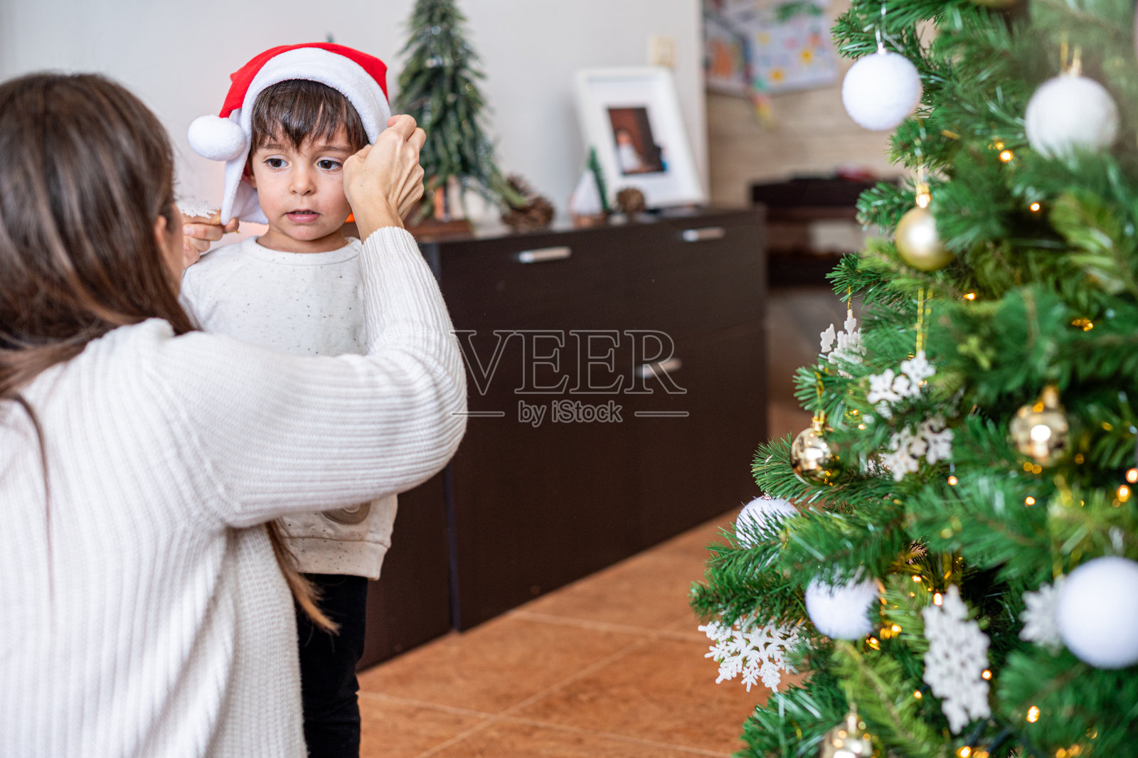 一位女性正在帮助一个孩子戴上红色帽子和白色衬衫。照片摄影图片
