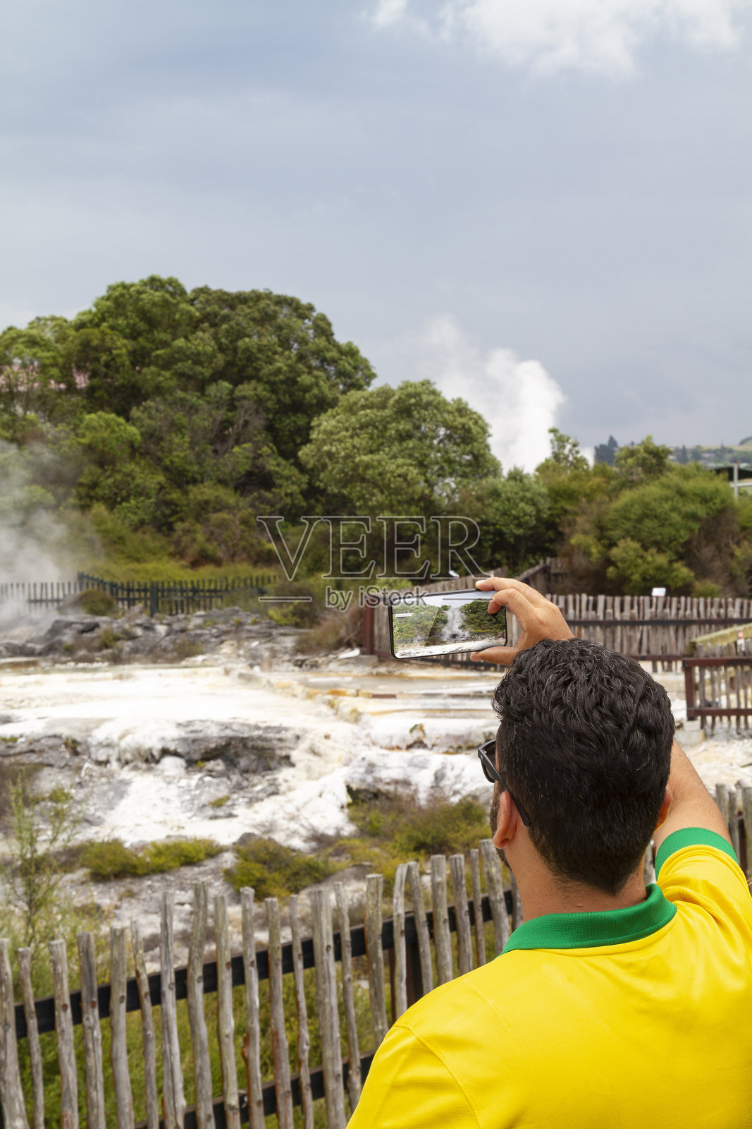 巴西拉丁男性游客在新西兰罗托鲁瓦用智能手机拍摄地热活动的壮丽景象,记录生动的自然风光和独特的文化。照片摄影图片