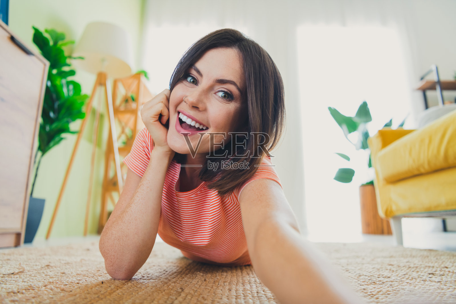 迷人的女孩在室内放松,穿着时尚的条纹T恤,阳光明媚的客厅里灿烂微笑。照片摄影图片