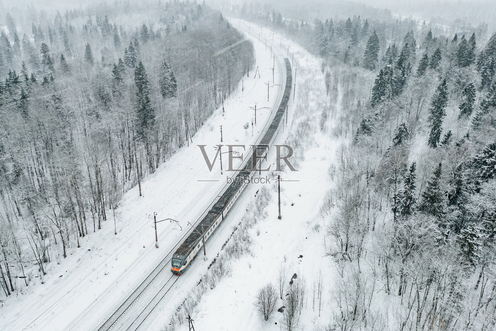 冬季森林中的雪地火车航拍视角。长途通勤列车驶向火车站。照片摄影图片