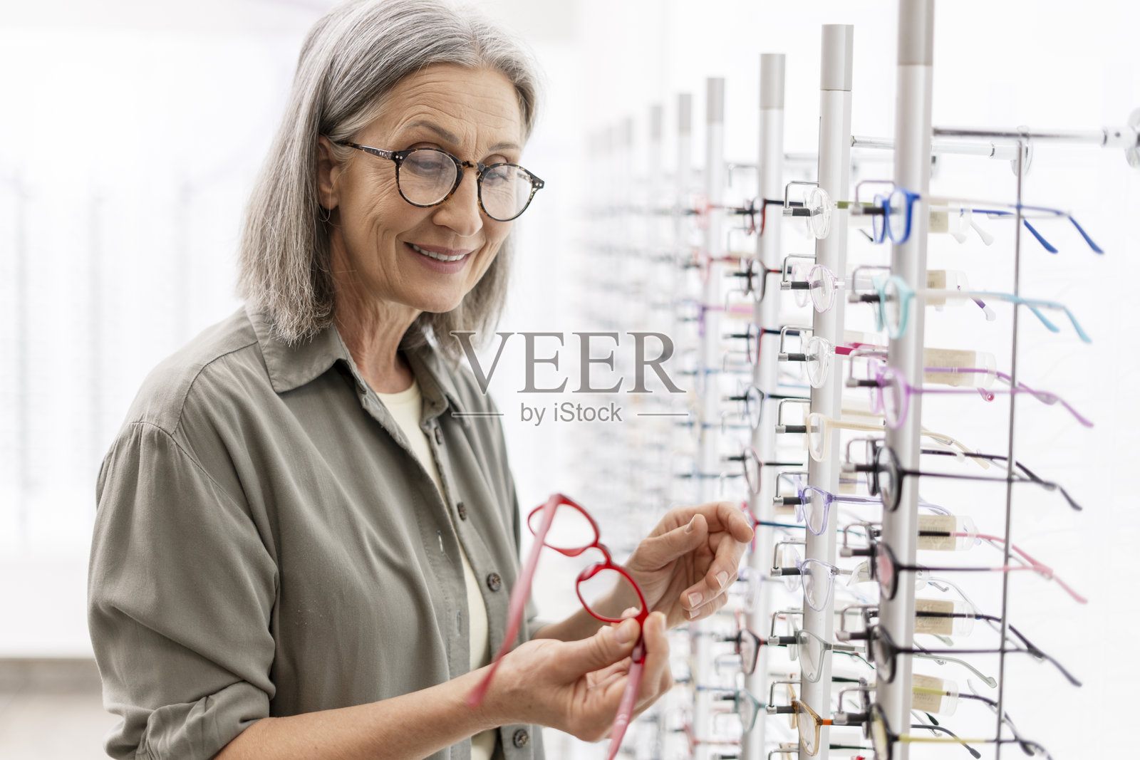 微笑的成熟的女性戴着时尚眼镜,在眼镜店挑选新框架照片摄影图片