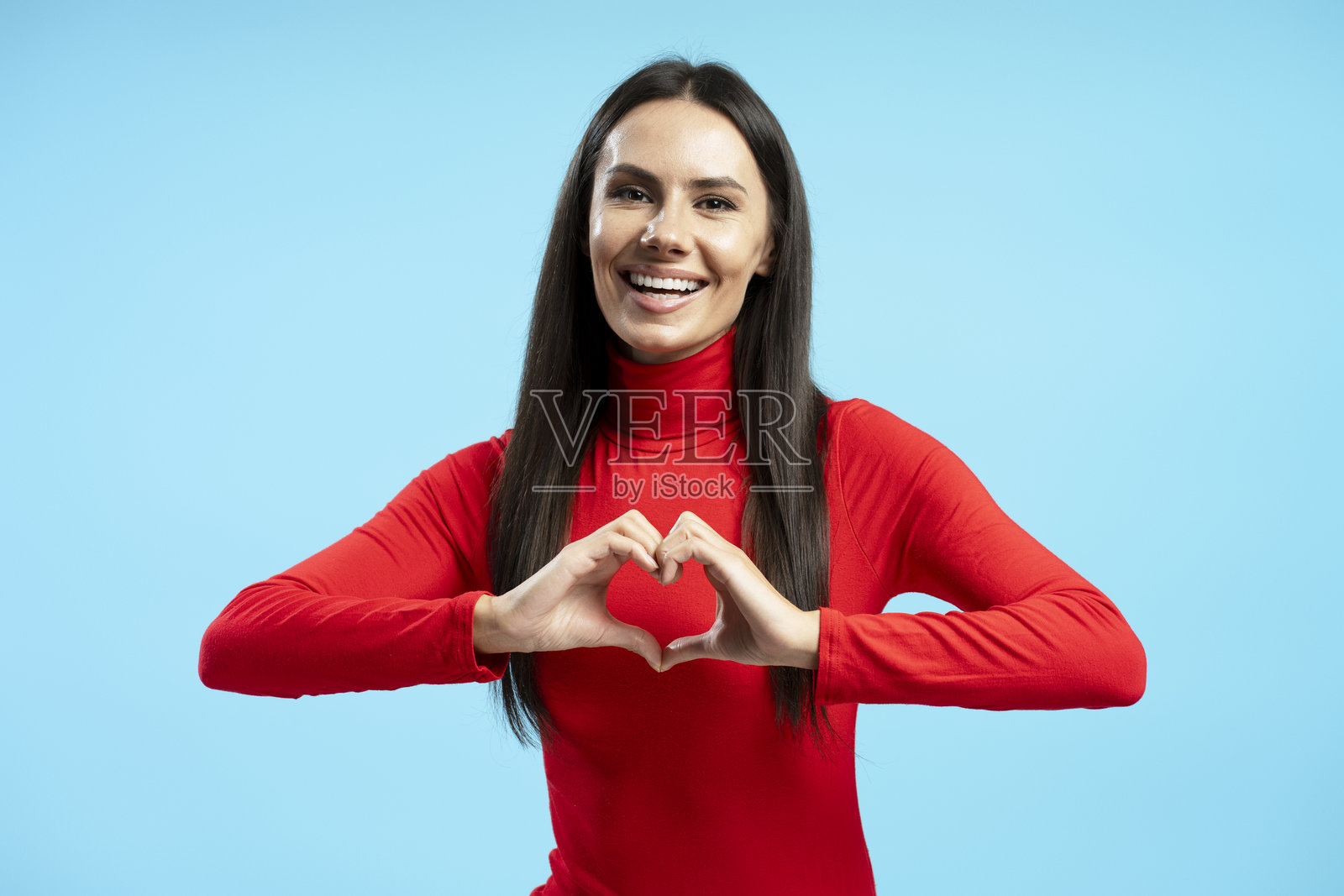 微笑的拉丁裔女性在蓝色背景下用手做出心形手势照片摄影图片