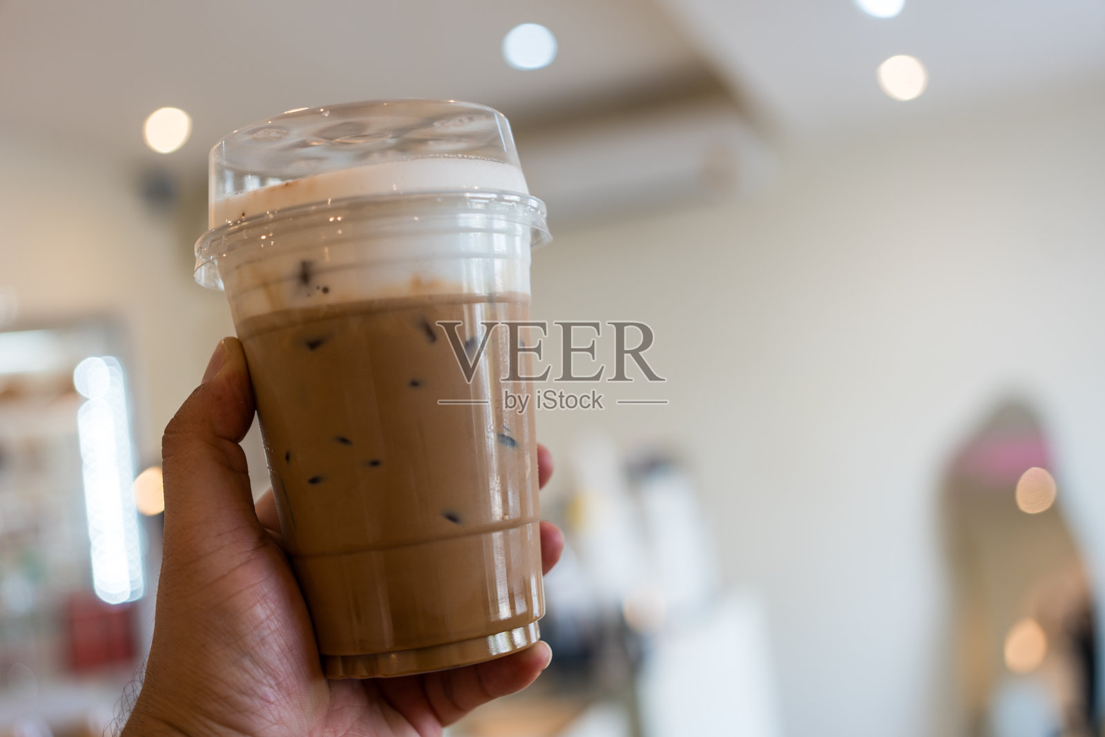 在咖啡店里手持菜单上最喜欢的饮品——冰摩卡,装在塑料杯中。照片摄影图片