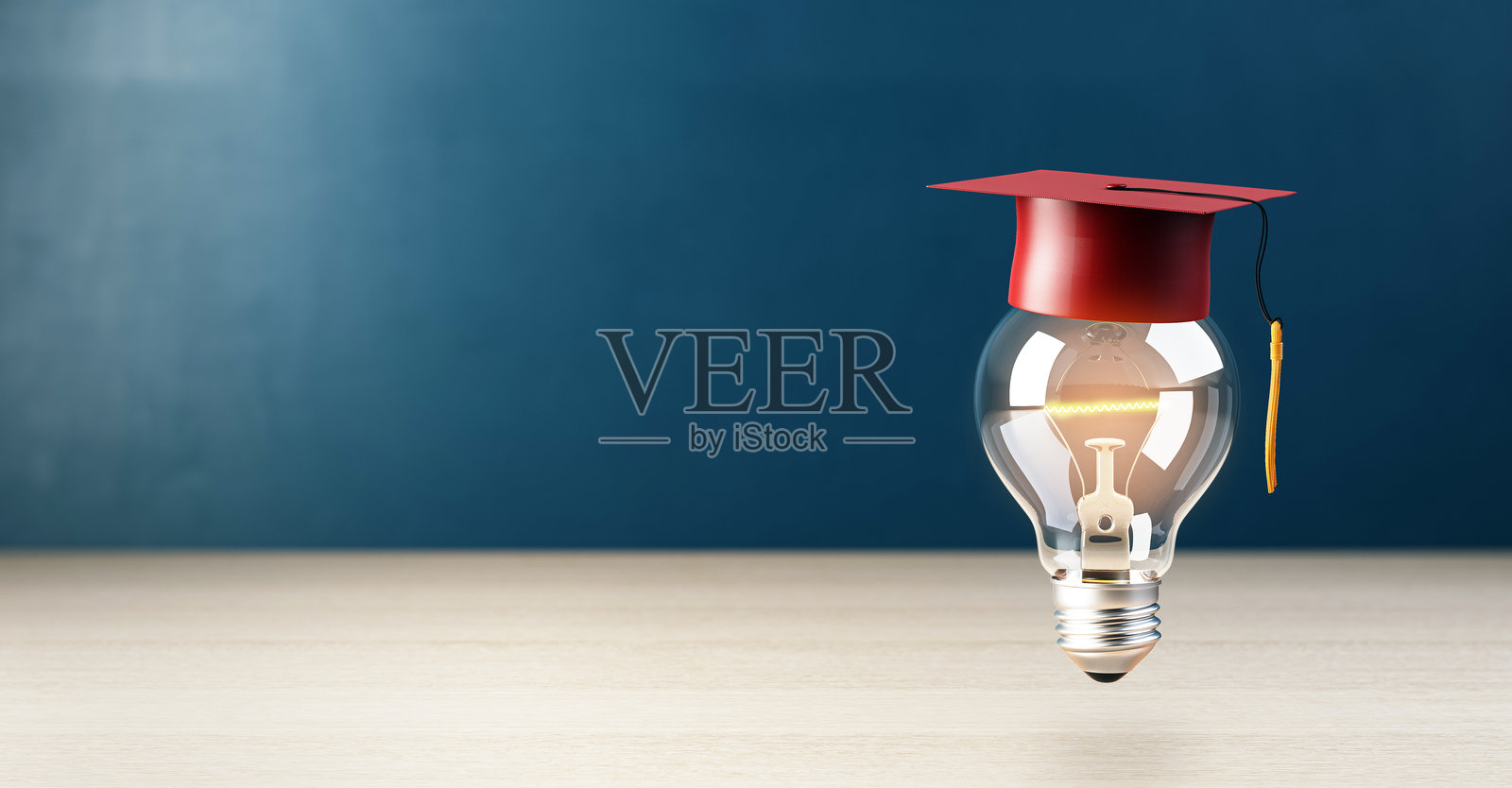 木桌上戴着红色毕业帽的灯泡,深蓝色背景。3D渲染。照片摄影图片